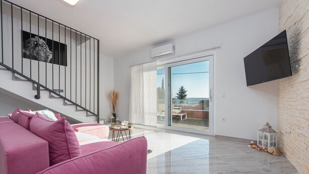 Una sala de estar moderna con un sofá rosa, una escalera, un ventanal con vistas y un televisor montado.