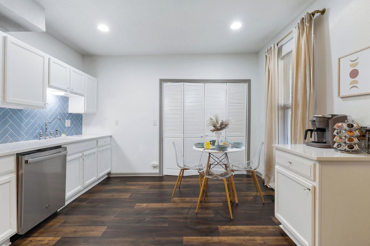 A modern kitchen with white cabinets, a dishwasher, and a dining area with a table and chairs.