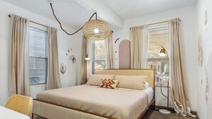 A bedroom with a bed, curtains, a hanging light fixture, and a window.