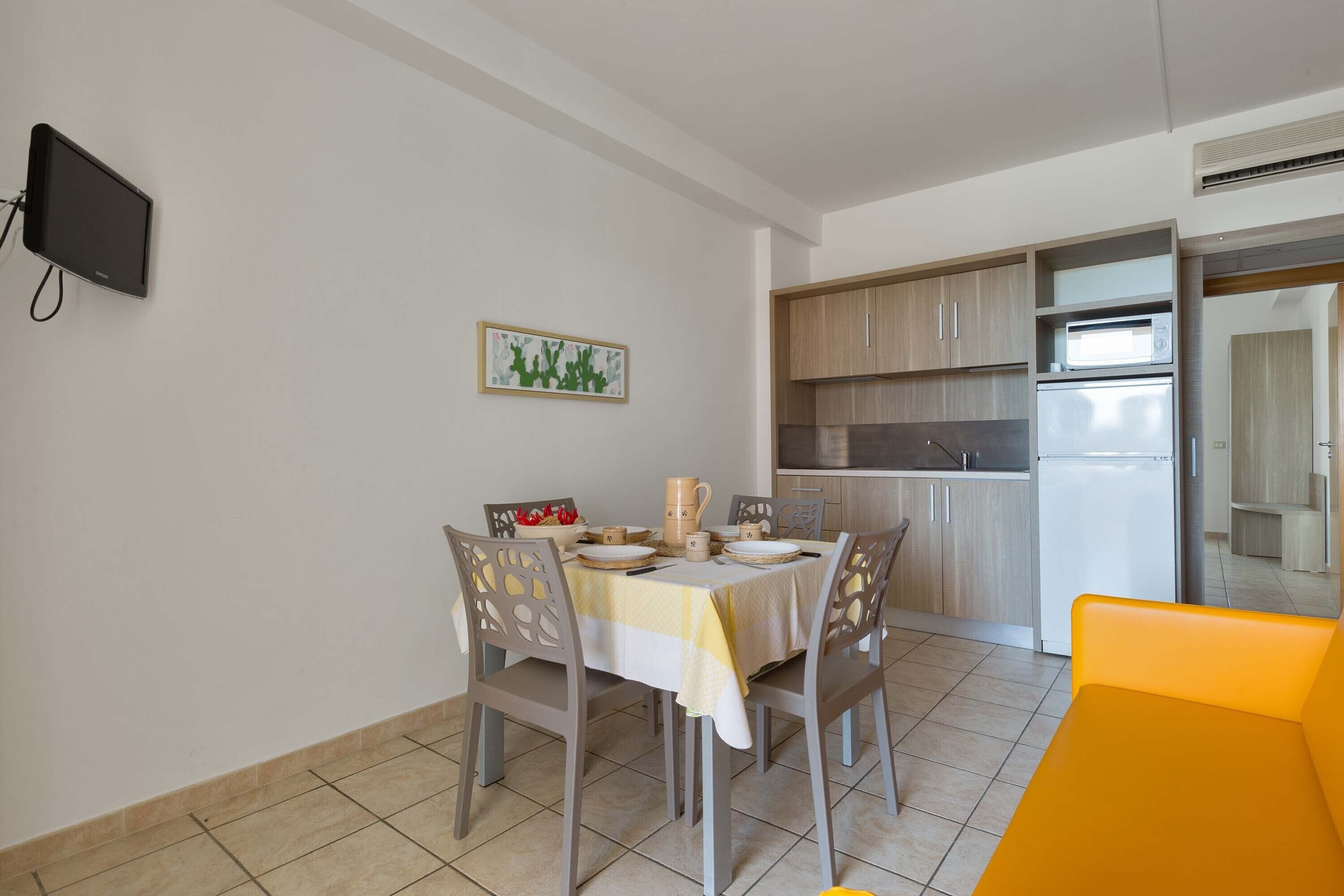 A compact kitchen with modern appliances, a dining area with a table set for two, and a TV mounted on the wall.