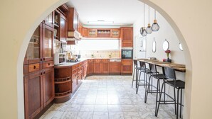 A kitchen with wooden cabinets, a marble floor, and a dining area with bar stools. - Supreme 4BR Villa With Garden & Sea View (Tel Aviv)