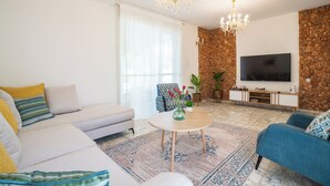 A modern living room with a sofa, armchairs, a coffee table, a TV, and a stone accent wall. - Supreme 4BR Villa With Garden & Sea View (Tel Aviv)