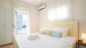 A hotel room with a bed, a window with curtains, an air conditioning unit, and a bedside table with a lamp. - Supreme 4BR Villa With Garden & Sea View (Tel Aviv)