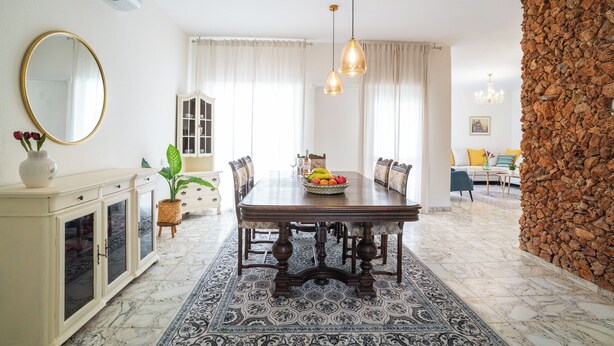 A dining area with a marble floor, a wooden dining table, and chairs. There is a buffet cabinet with glass doors, a mirror, and a vase with flowers. - Supreme 4BR Villa With Garden & Sea View (Tel Aviv)