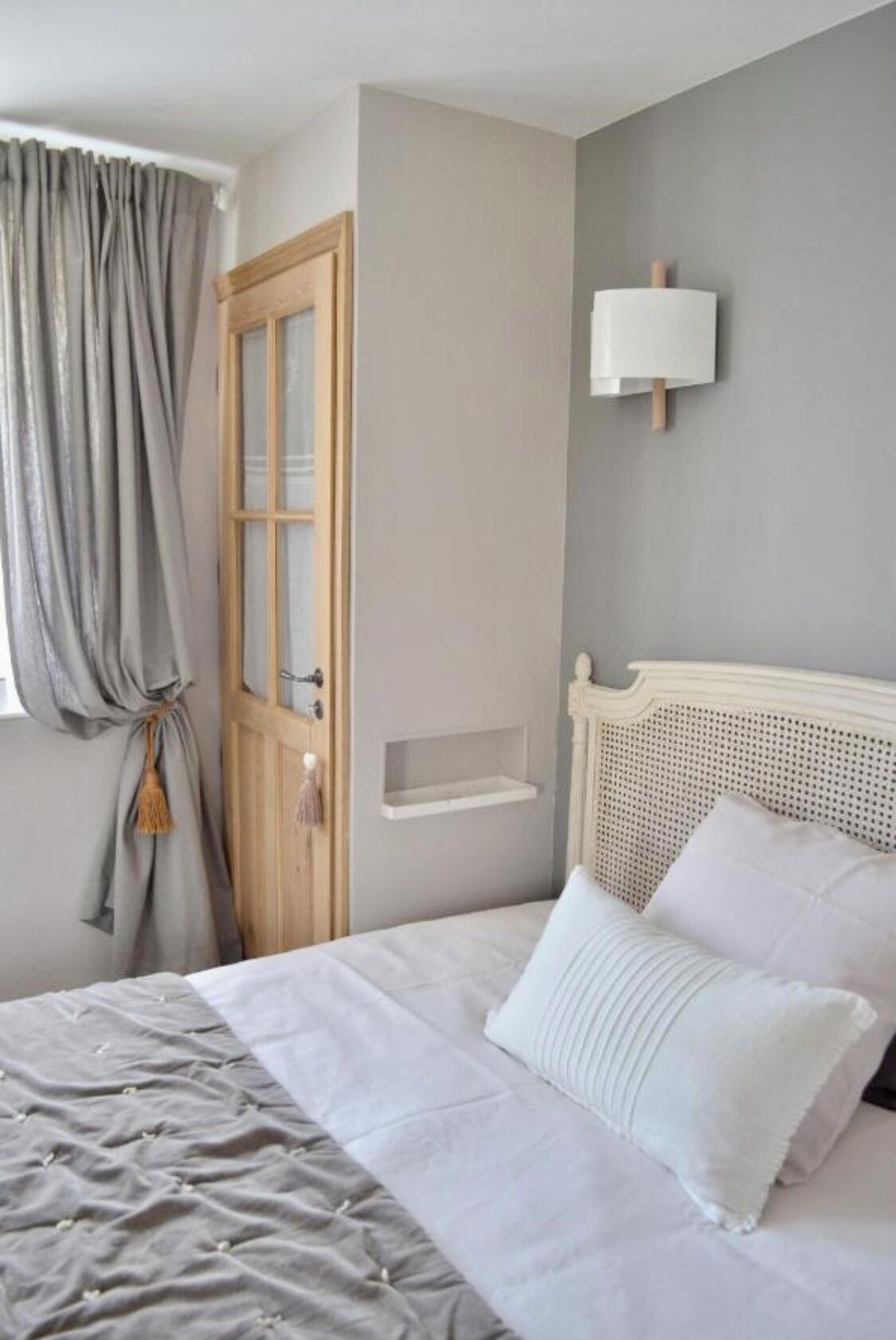 Un dormitorio con una cama, un armario de madera, una estantería en la pared y una ventana con cortinas.