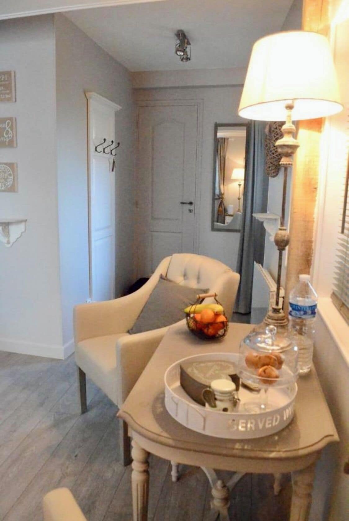 Een eetgedeelte met een tafel gedekt voor twee personen, een lamp, een fruitmand en een dienblad met een taart en een kaars.