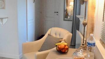 Een eetgedeelte met een tafel gedekt voor twee personen, een lamp, een fruitmand en een dienblad met een taart en een kaars.