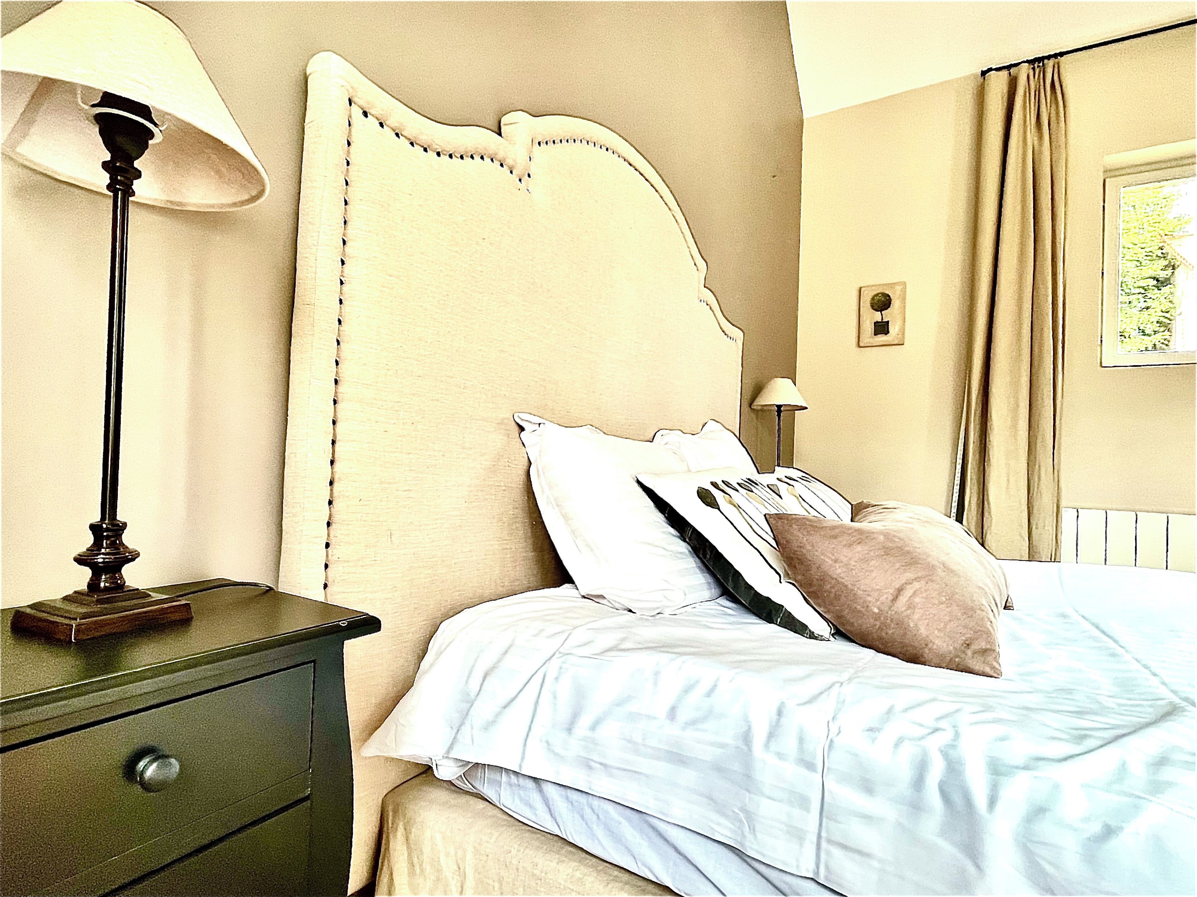 Une chambre à coucher avec un lit, une table de chevet, une lampe et une fenêtre avec des rideaux.