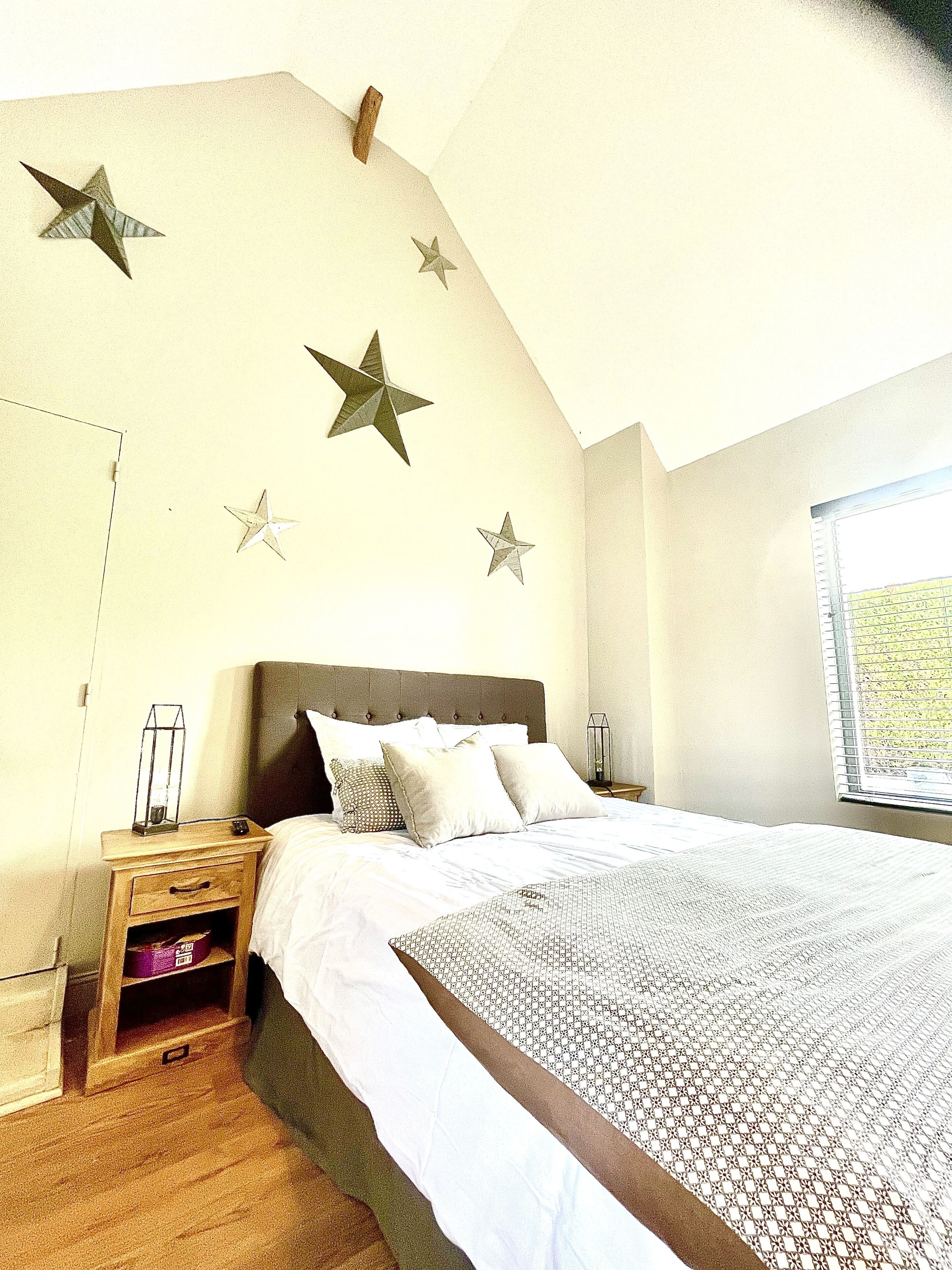 A bedroom with a large bed, wooden nightstand, and a window with blinds.