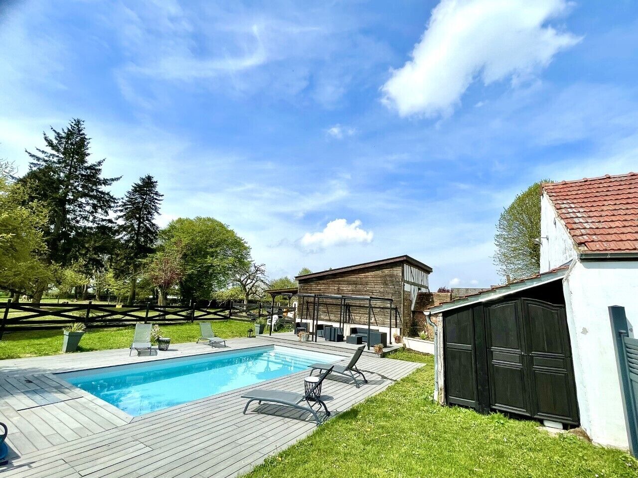 Un patio trasero con piscina, terraza de madera y un cobertizo pequeño.