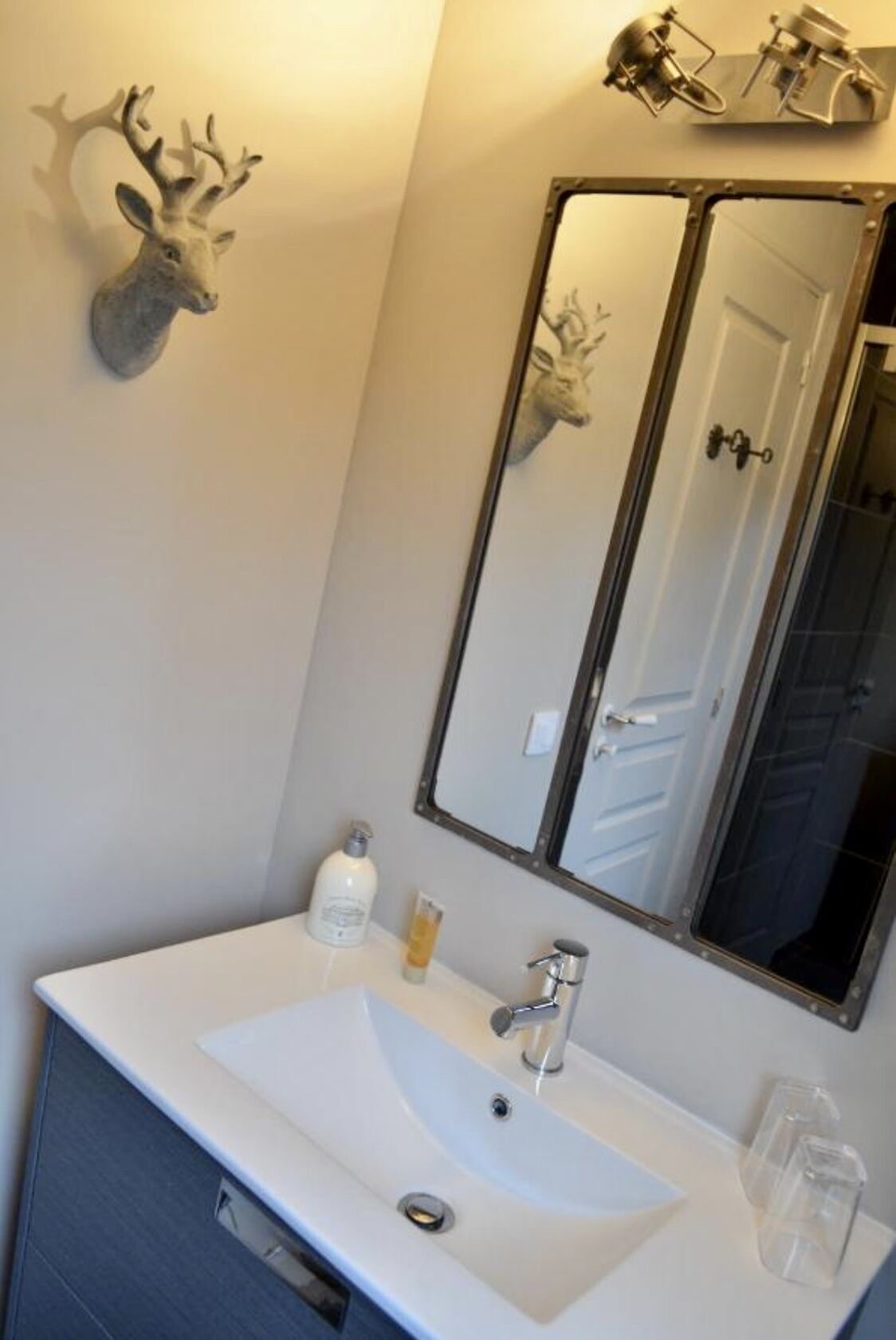 Een badkamer met een wit wastafelmeubel, een spiegel en een op de muur bevestigde hertenkop.