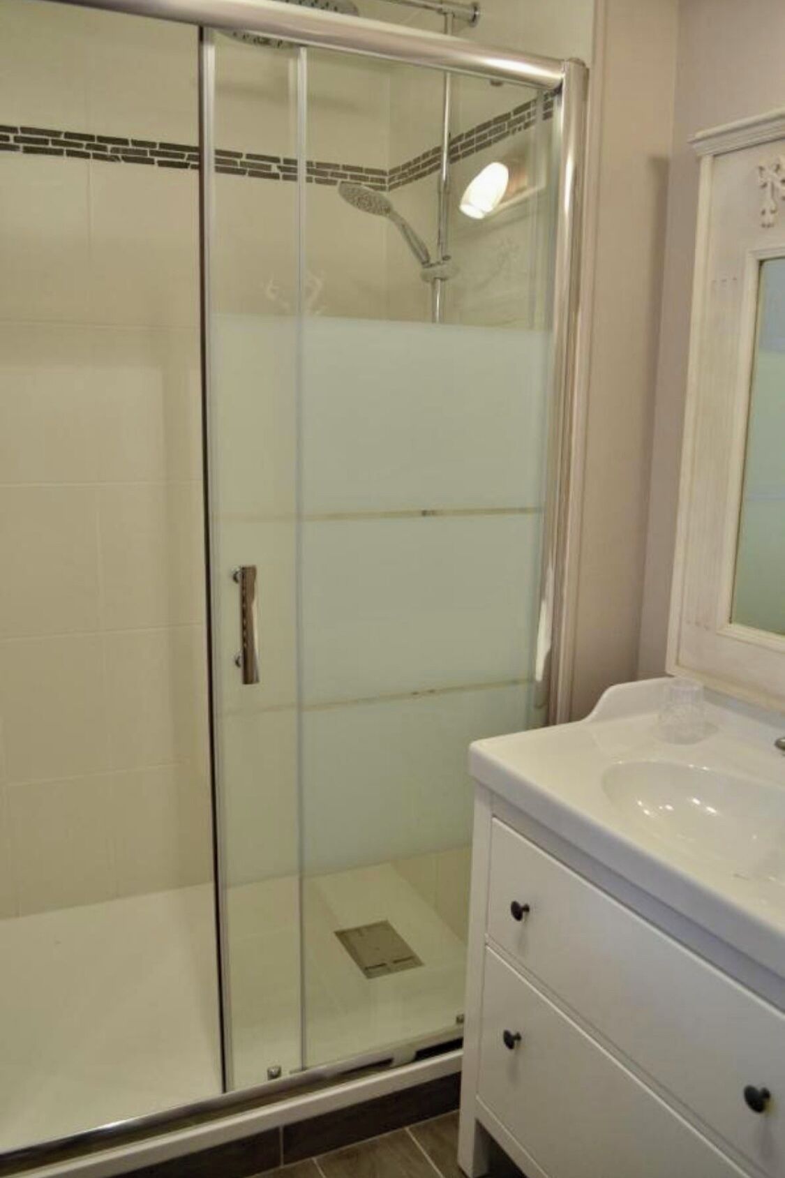 A bathroom with a glass-enclosed shower, a white sink, and a vanity with drawers.