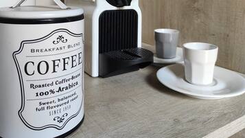 Una macchina da caffè, un contenitore per caffè e due tazze su un piano di legno.