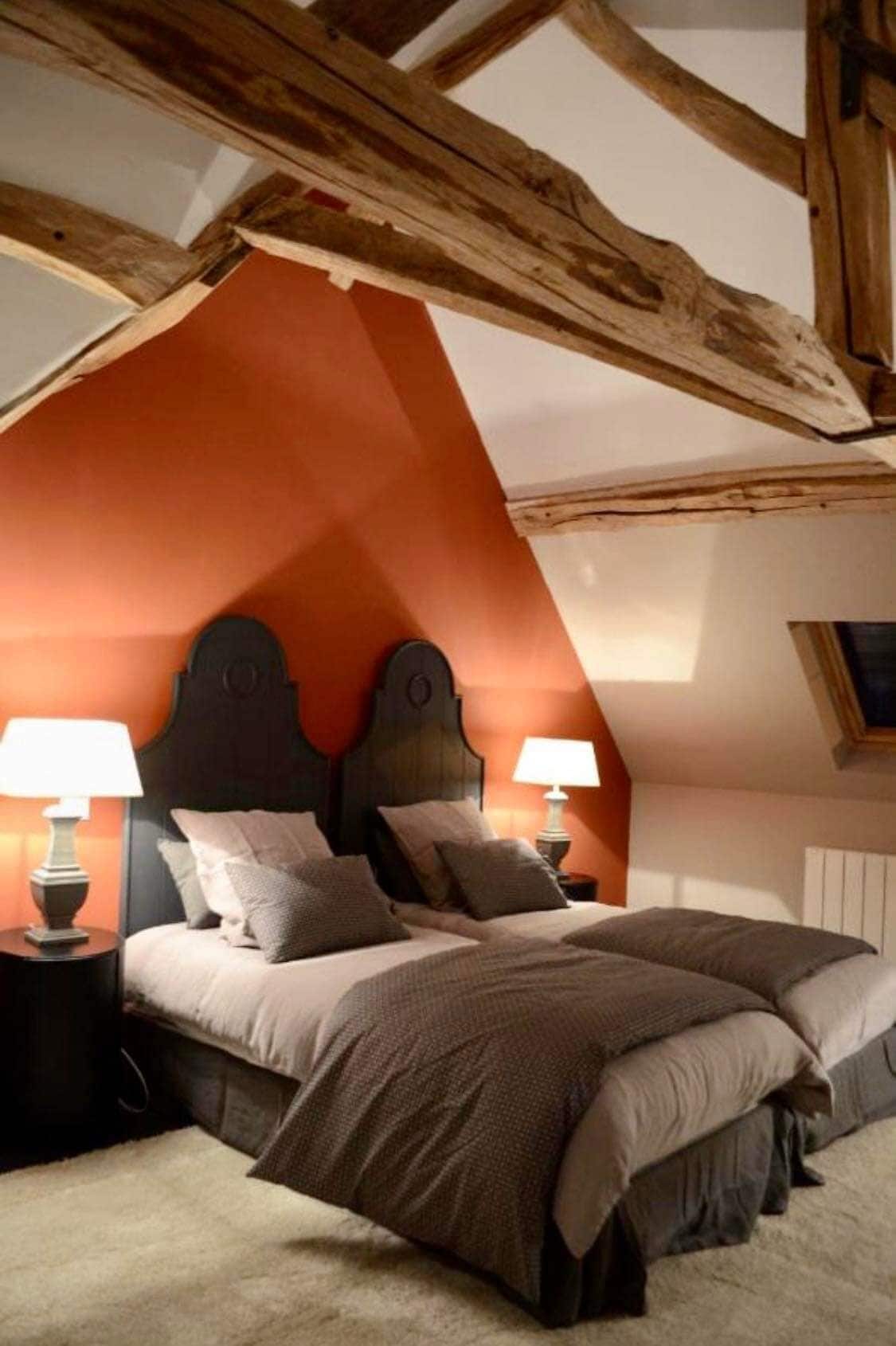 Un dormitorio con techo inclinado, una cama con múltiples almohadas, dos lámparas de noche y un cabecero de madera.