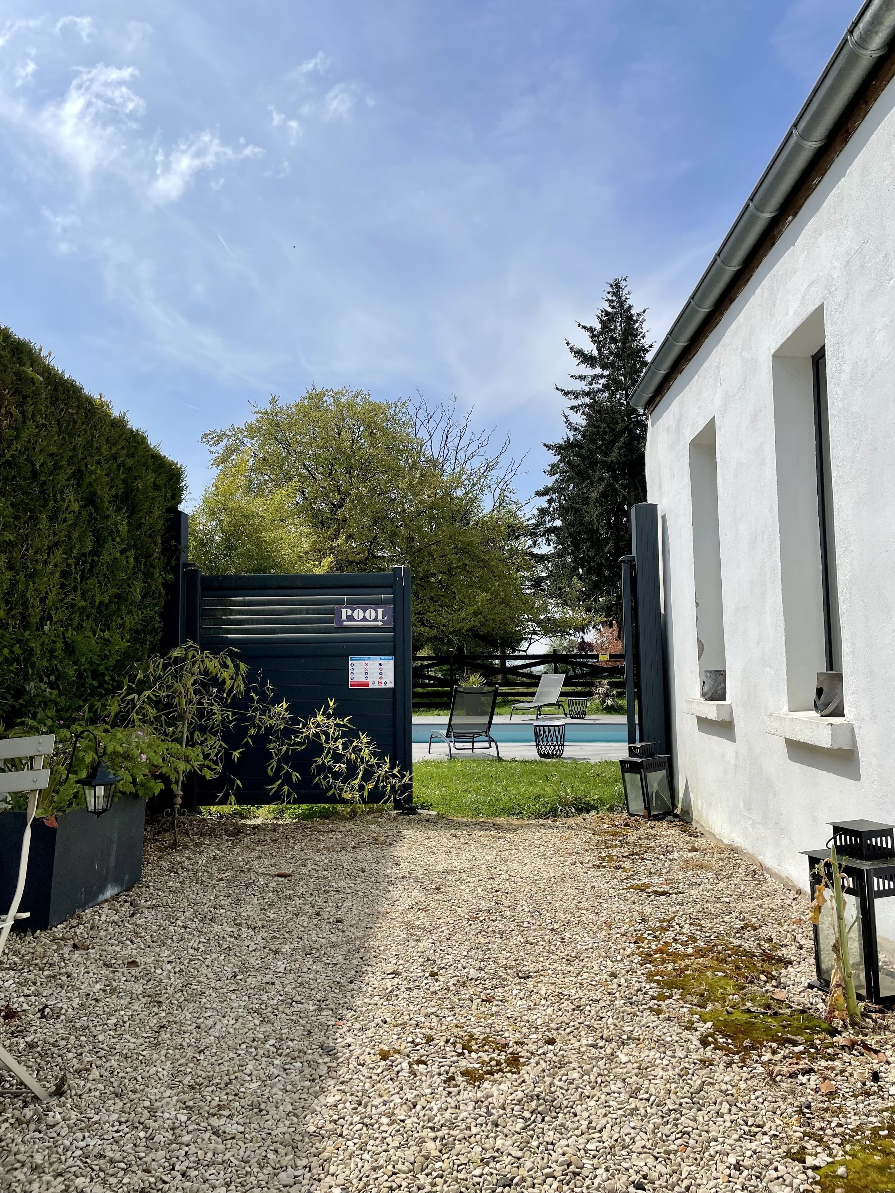 Un patio de grava con piscina, una zona de estar cubierta y un edificio de fachada blanca.