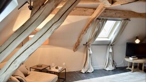 A cozy attic bedroom with a sloped ceiling, a single bed, a small table, a TV, and a window with curtains. - Le Paddock (La Drenne)