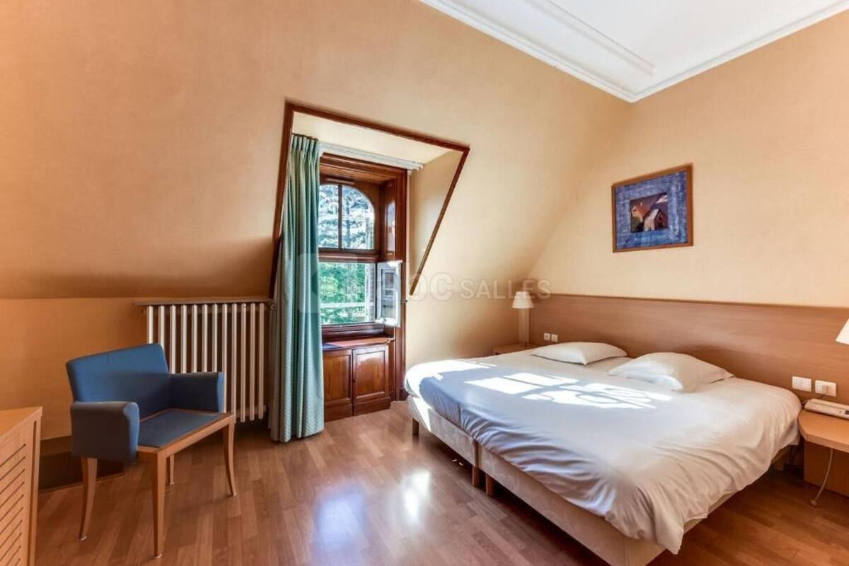 Ein Schlafzimmer mit einem Bett, einem Sessel, einem Heizkörper, einem Fenster mit Vorhängen und einem Bild an der Wand.