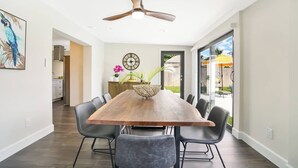 Un comedor moderno con una mesa de madera, sillas negras, un ventilador de techo y un reloj grande en la pared.