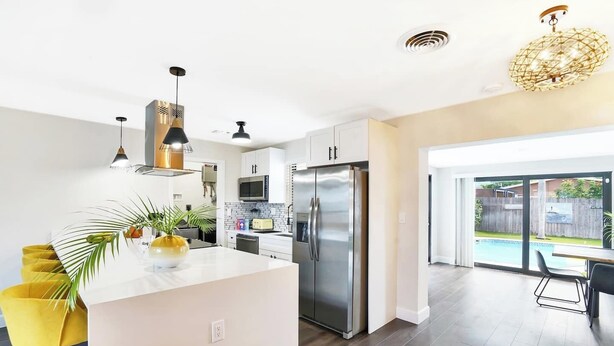 Una cocina moderna con una isla central, electrodomésticos de acero inoxidable y vista a un patio trasero con piscina.