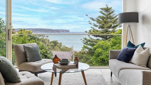 Una sala de estar moderna con una mesa de vidrio, dos sofás y vista al mar y acantilados.