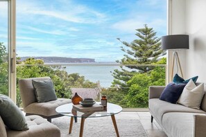 Una sala de estar moderna con una mesa de vidrio, dos sofás y vista al mar y acantilados.