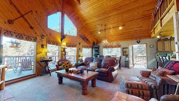 Un intérieur de chalet chaleureux avec un plafond en bois, de grandes fenêtres, une cheminée et un coin repas.