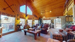 Interior acogedor de una cabaña con techo de madera, ventanas amplias, chimenea y zona de comedor.