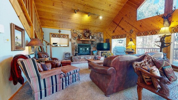 Interior acogedor de una cabaña con chimenea de piedra, mobiliario de cuero y televisor montado.