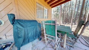 Una cabaña de madera con un espacio de estar al aire libre cubierto, una ventana y vistas a un bosque.