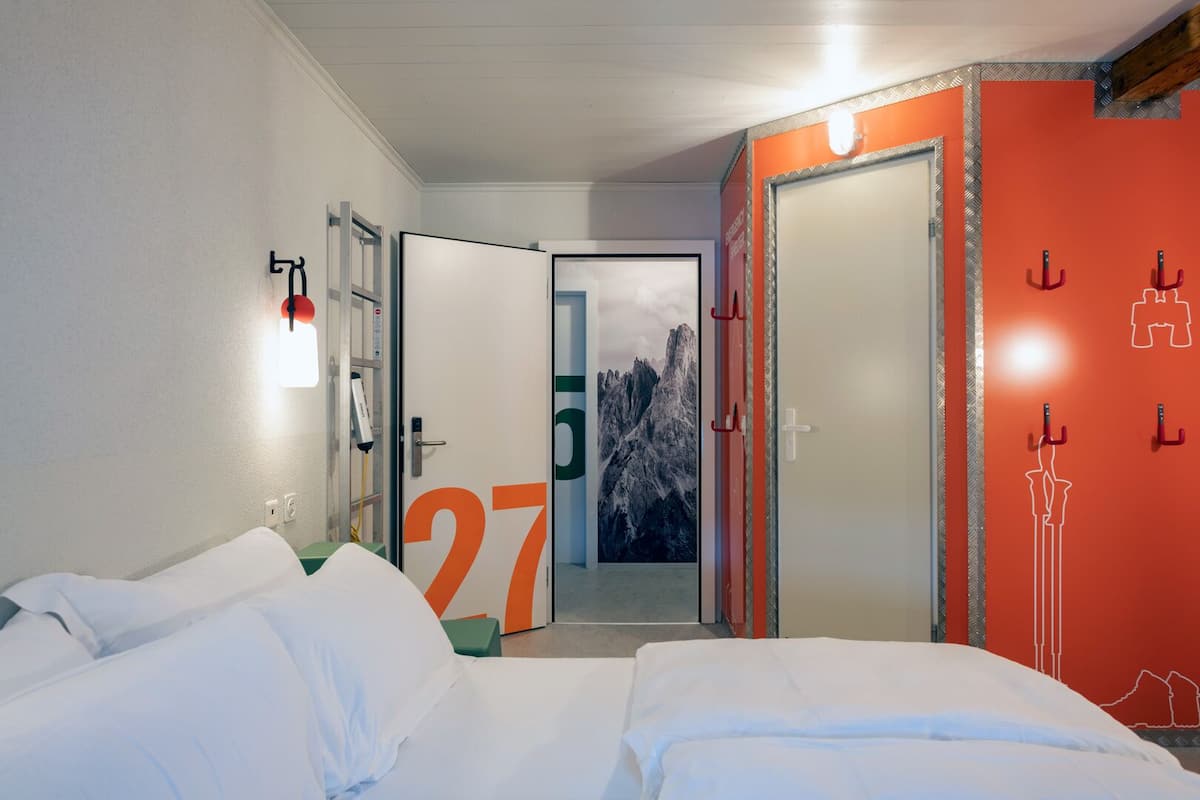 A hotel room with a bed, a bathroom with a shower, and a door leading to a corridor.