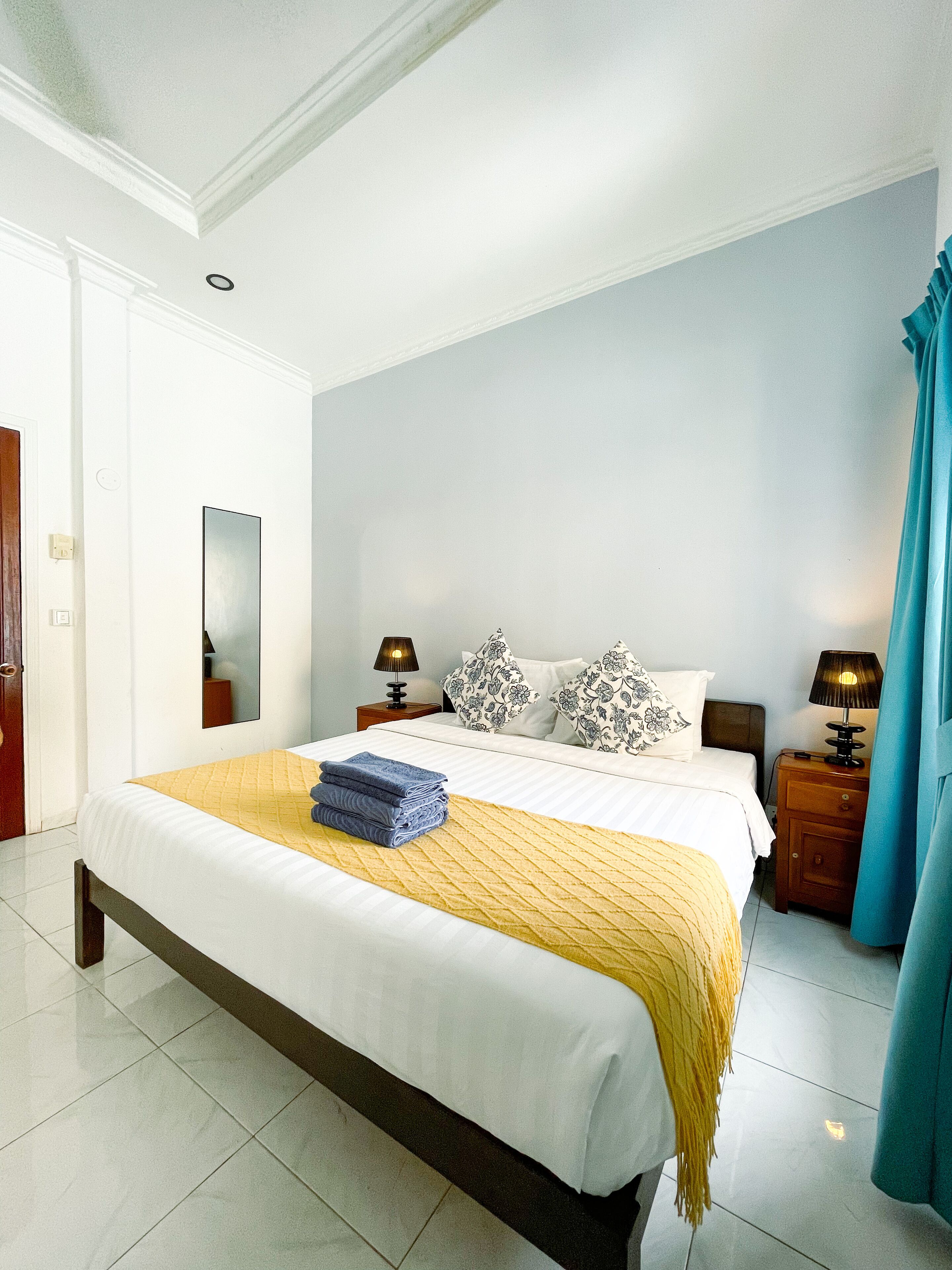 A neatly made bed with a yellow throw, two bedside lamps, and a mirror on the wall.