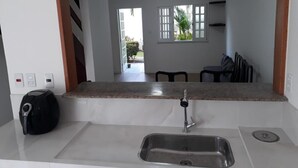 A kitchen with a granite countertop, stainless steel sink, and a kettle. There is a window with a view of a patio and greenery. - Village Duplex, 2 Bedrooms, 100m from the Beach with Pool (Salvador)
