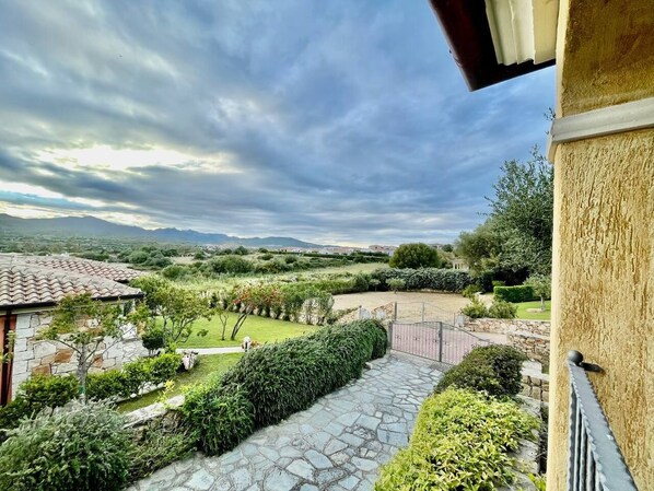 A stone pathway leading to a courtyard with a view of distant mountains and a cloudy sky.