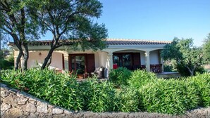 A Mediterranean-style villa with a tiled roof, a covered patio with outdoor furniture, and lush greenery. - House / Villa - Budoni (Tanaunella (Budoni))