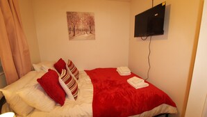 Ein Hotelzimmer mit Bett, einem an der Wand befestigten Fernseher und einem Gemälde über dem Bett.