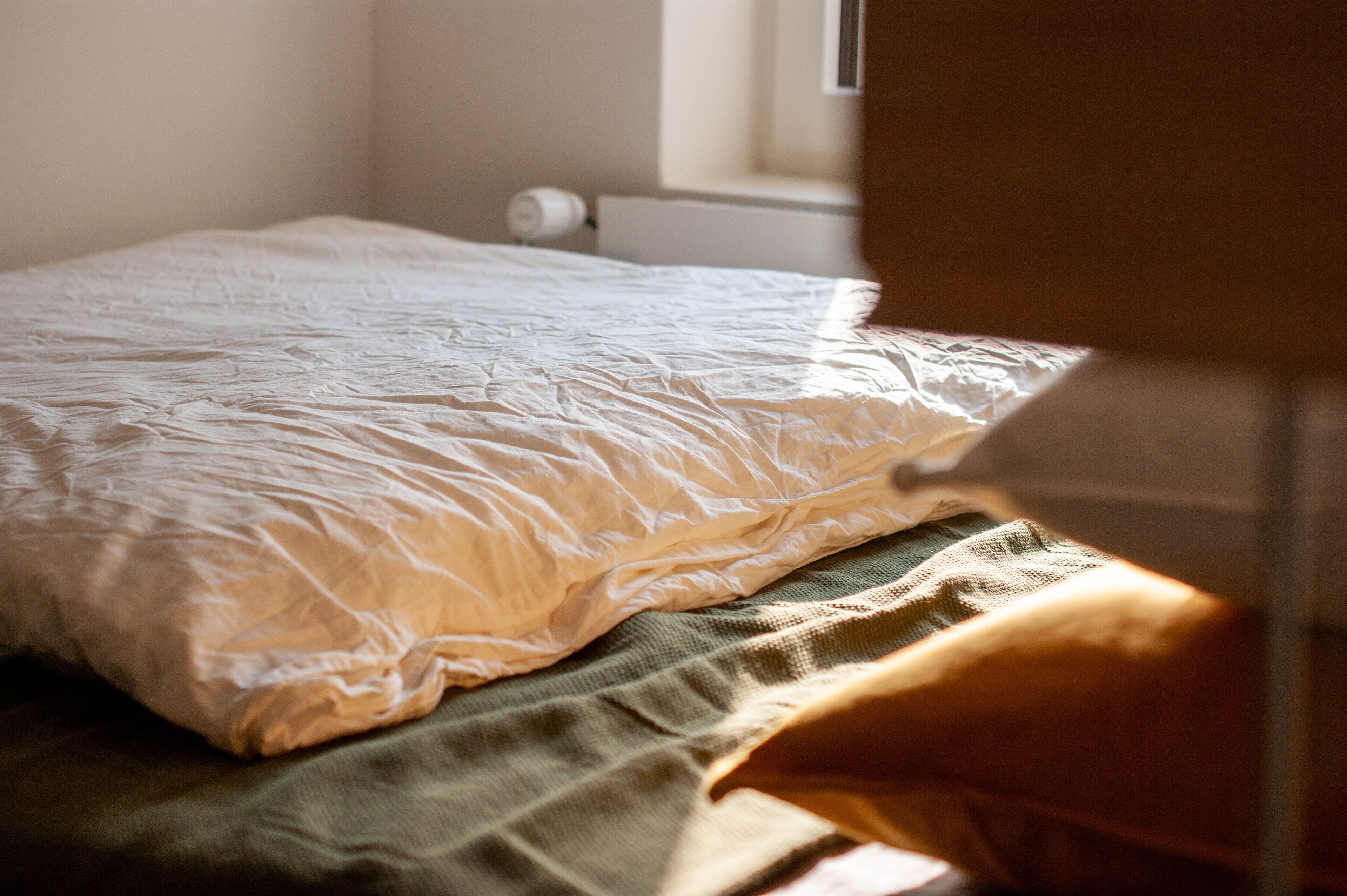 Un lit avec une couette blanche et un plaid vert.