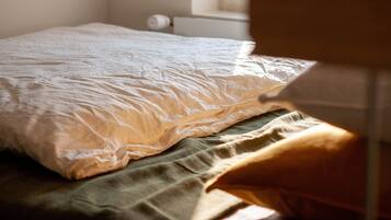 Un lit avec une couette blanche et un plaid vert.