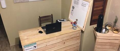 A reception desk with a computer, a small chair, a trash bin, and a wooden cabinet with decorative items.