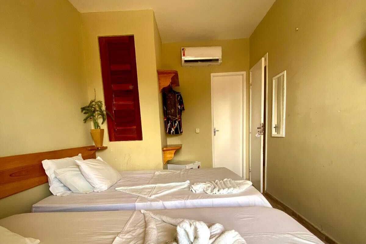 Quarto de hotel com duas camas, uma persiana vermelha, um ar condicionado e um vaso de planta.