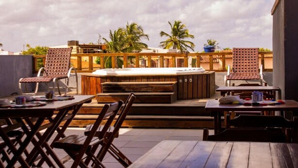An outdoor patio with wooden furniture, a hot tub, and palm trees in the background. - Pousada Aguia da Vila (Jijoca de Jericoacoara)