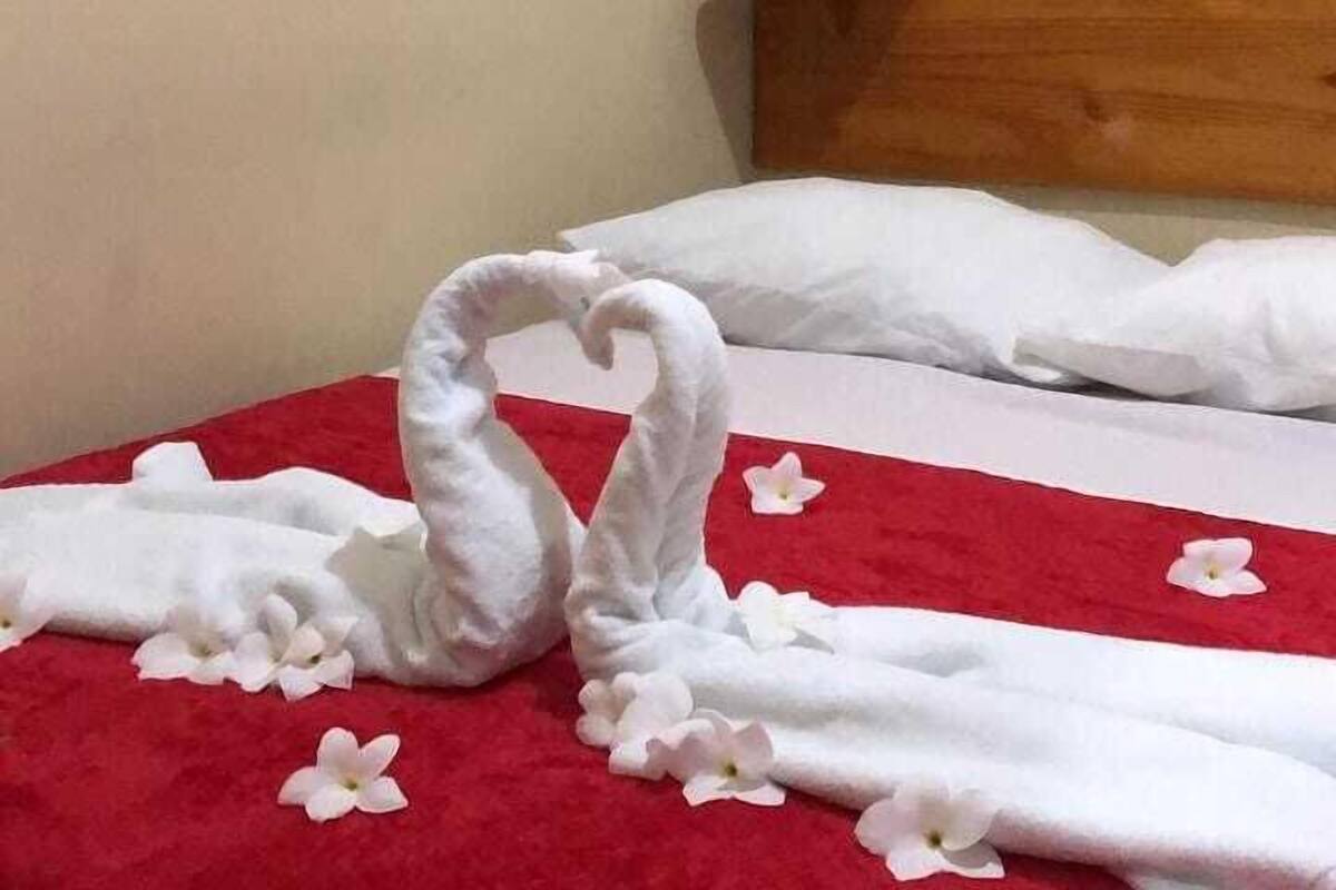 Cama com travesseiros brancos e manta vermelha, decorada com flores brancas.