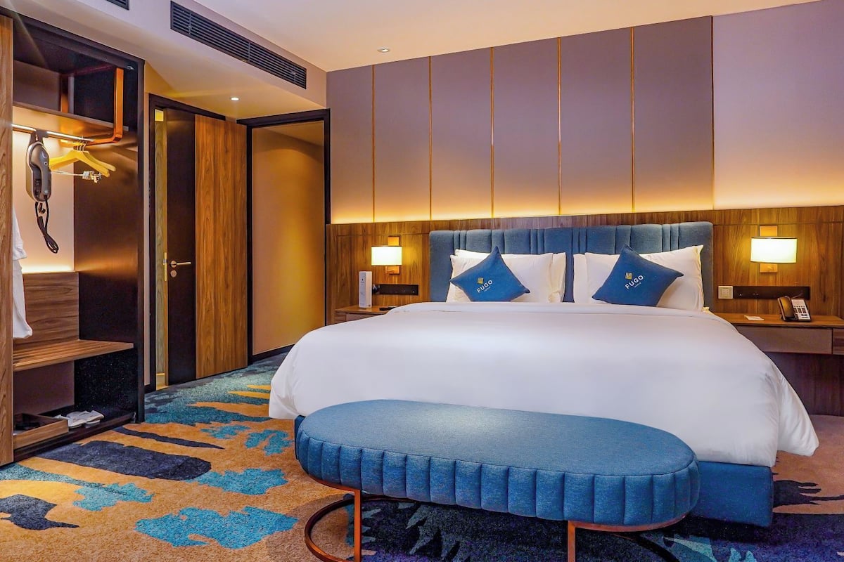 Ein Hotelzimmer mit einem großen Bett, einem Holzschrank, einer Bank und einem Nachttisch mit Lampe.
