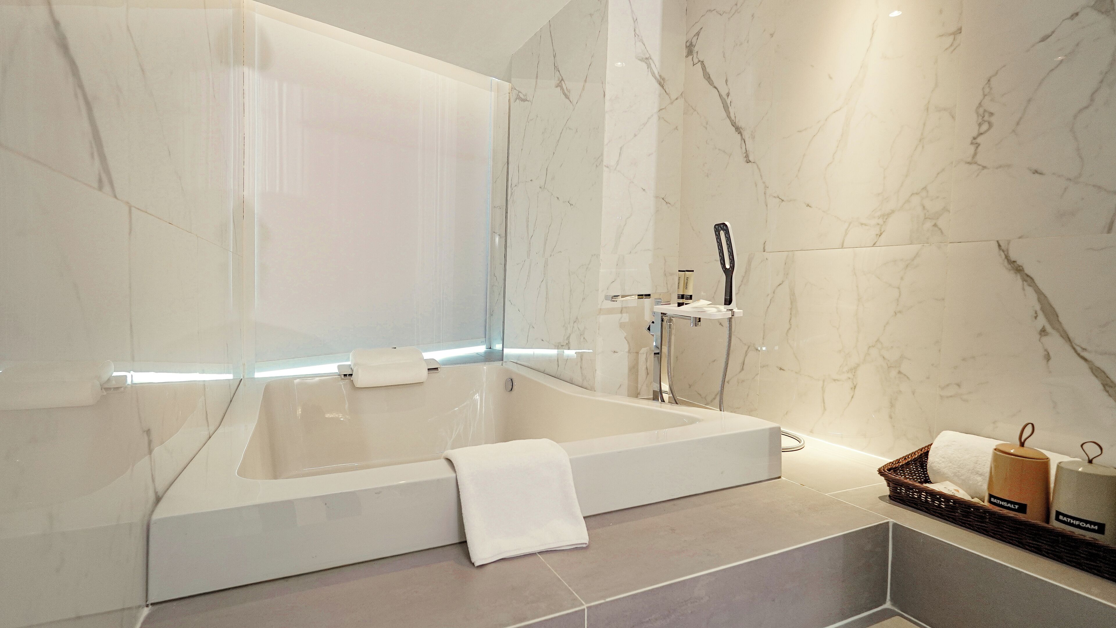 A modern bathroom with a large bathtub, a glass shower enclosure, and marble walls.