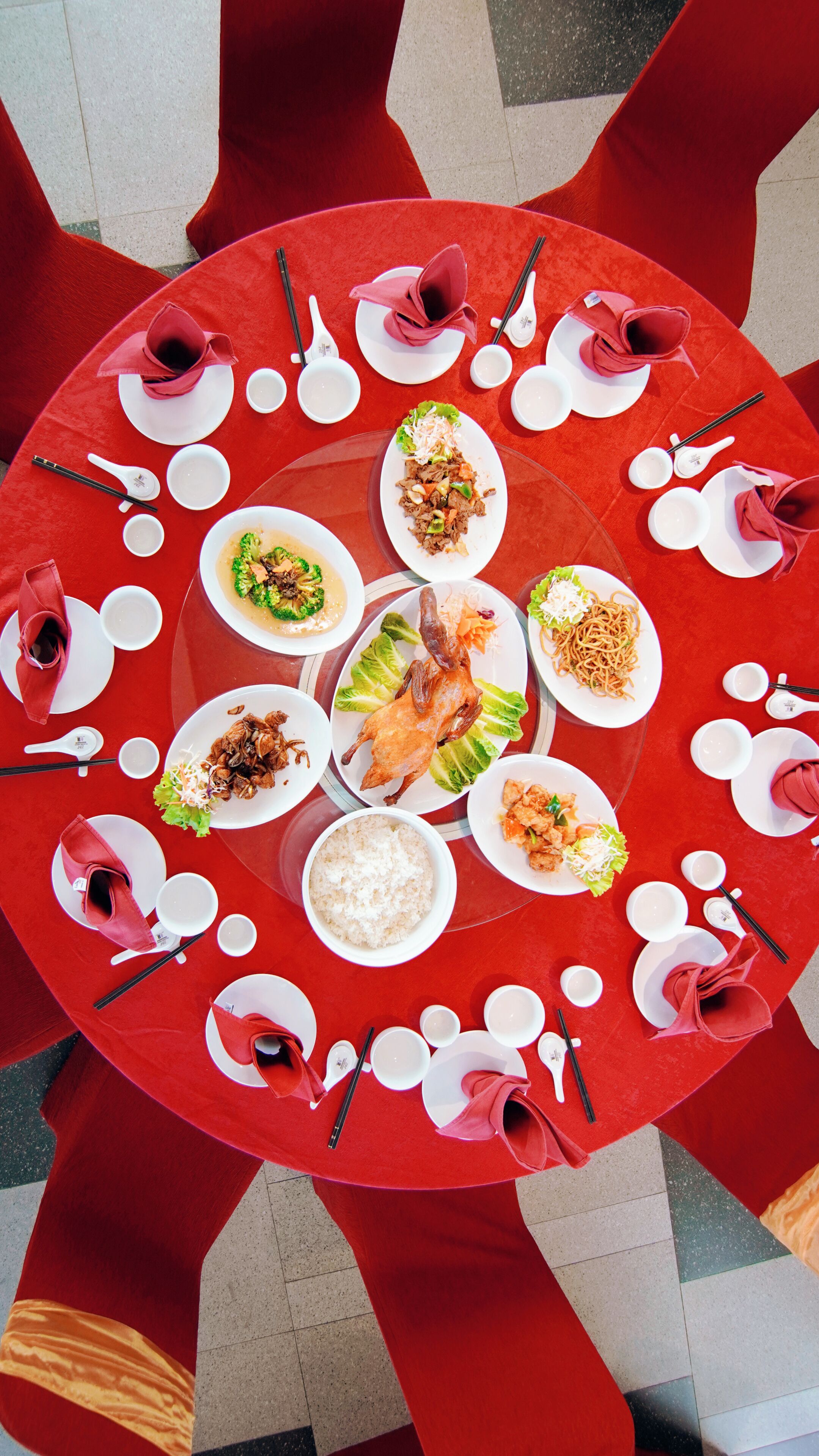Une table ronde, sur laquelle sont disposés divers plats et ustensiles, entourée de chaises rouges.