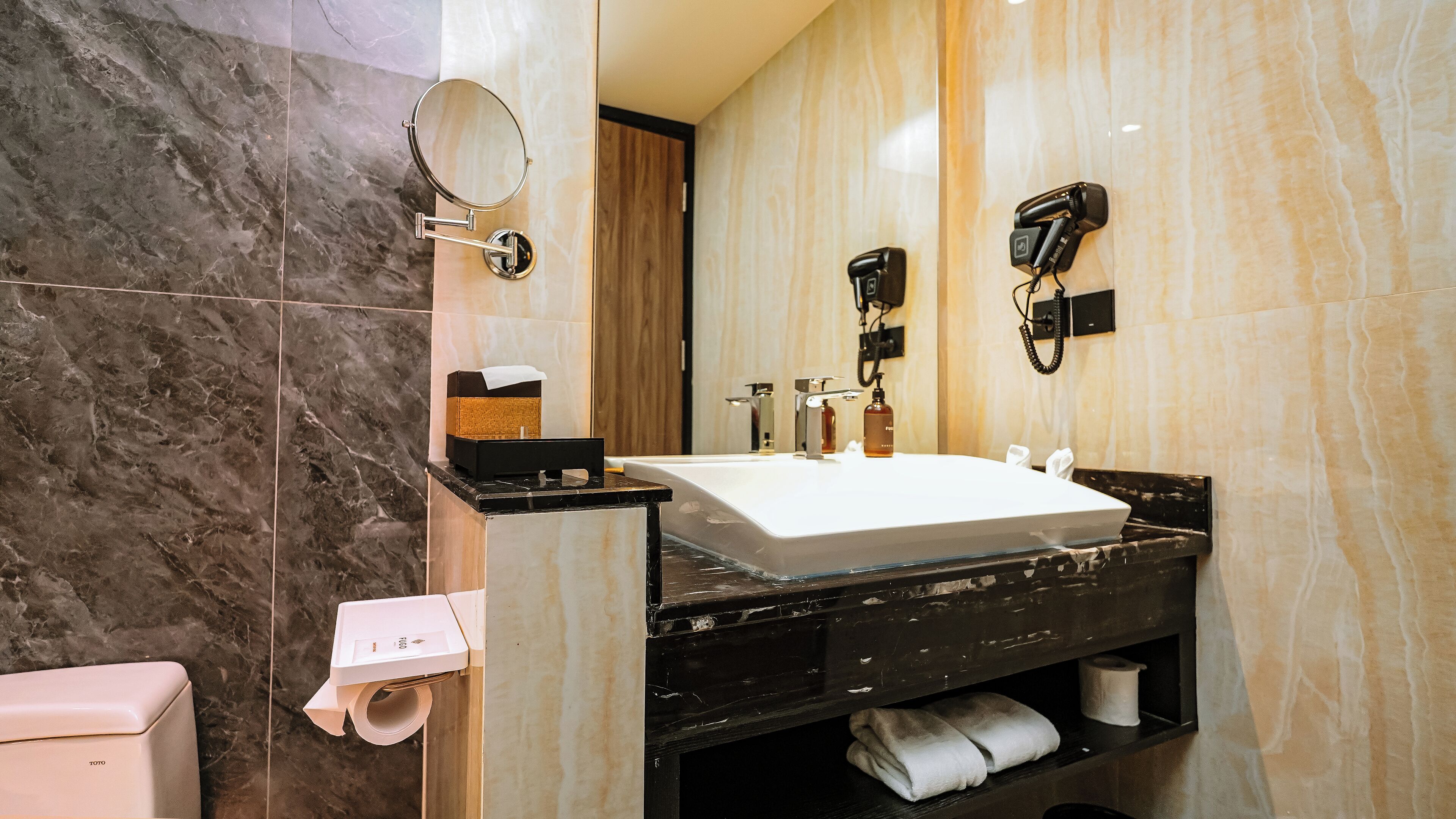 Un baño moderno con tocador de mármol, un espejo grande, un secador de pelo y un perchero para toallas.