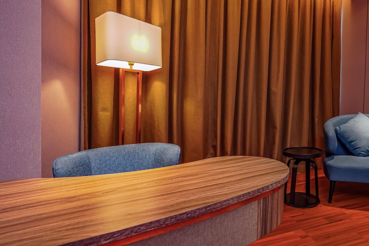 A reception area with a wooden reception desk, a blue armchair, a small round table, and a lamp.