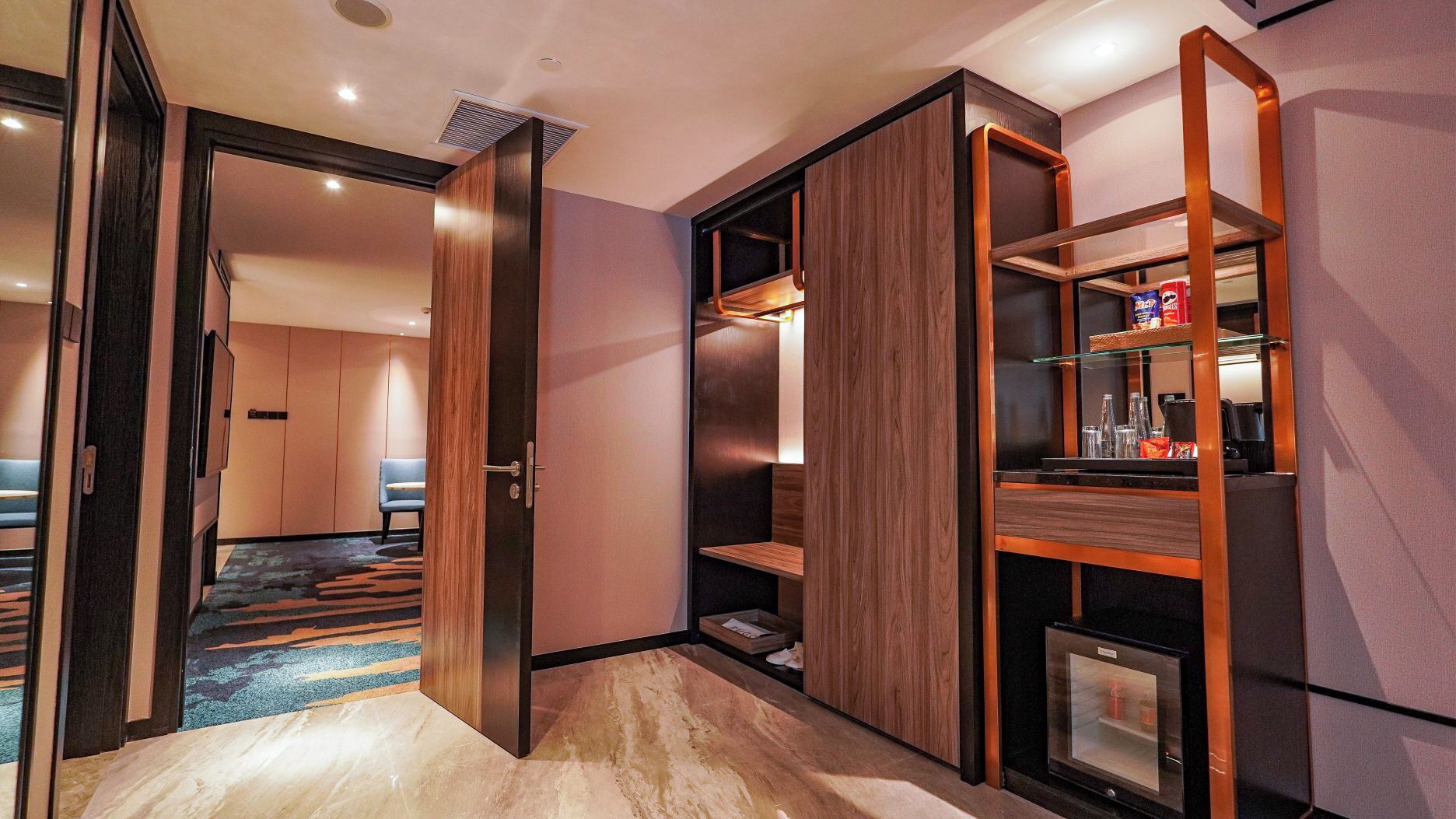 Ein modernes Hotelzimmer mit einer Schiebetür, einer Minibar und einer Sitzecke mit blauem Sessel.