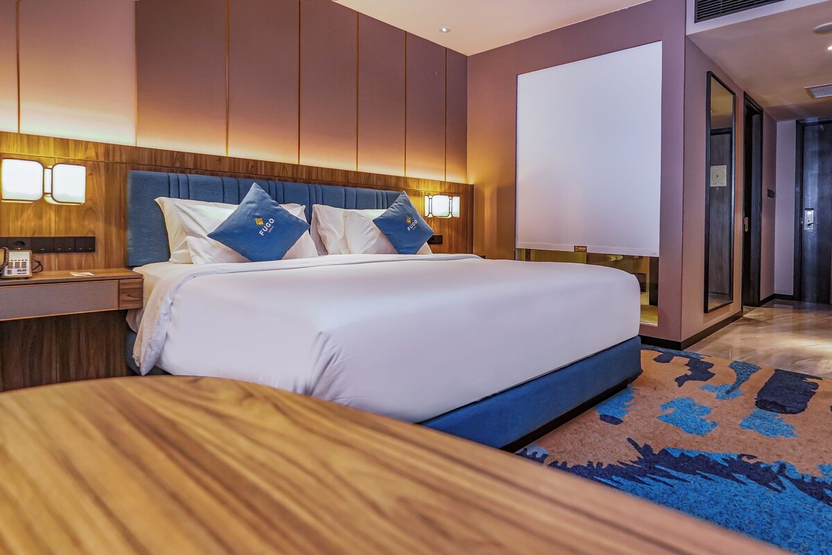 Habitación de hotel con una cama grande, cabecero de madera, mesitas de noche y una alfombra azul estampada.