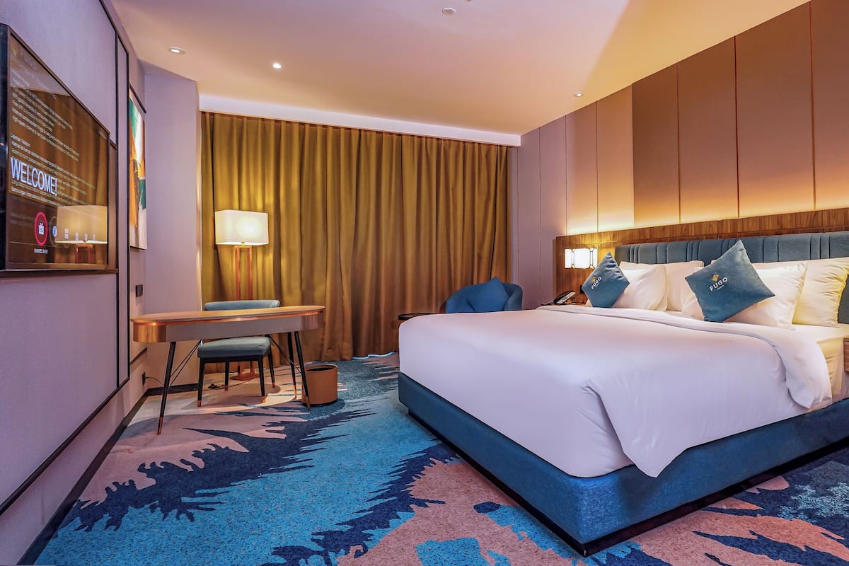 Ein Hotelzimmer mit einem großen Bett, einem Schreibtisch, einem Stuhl und einem Fernseher.