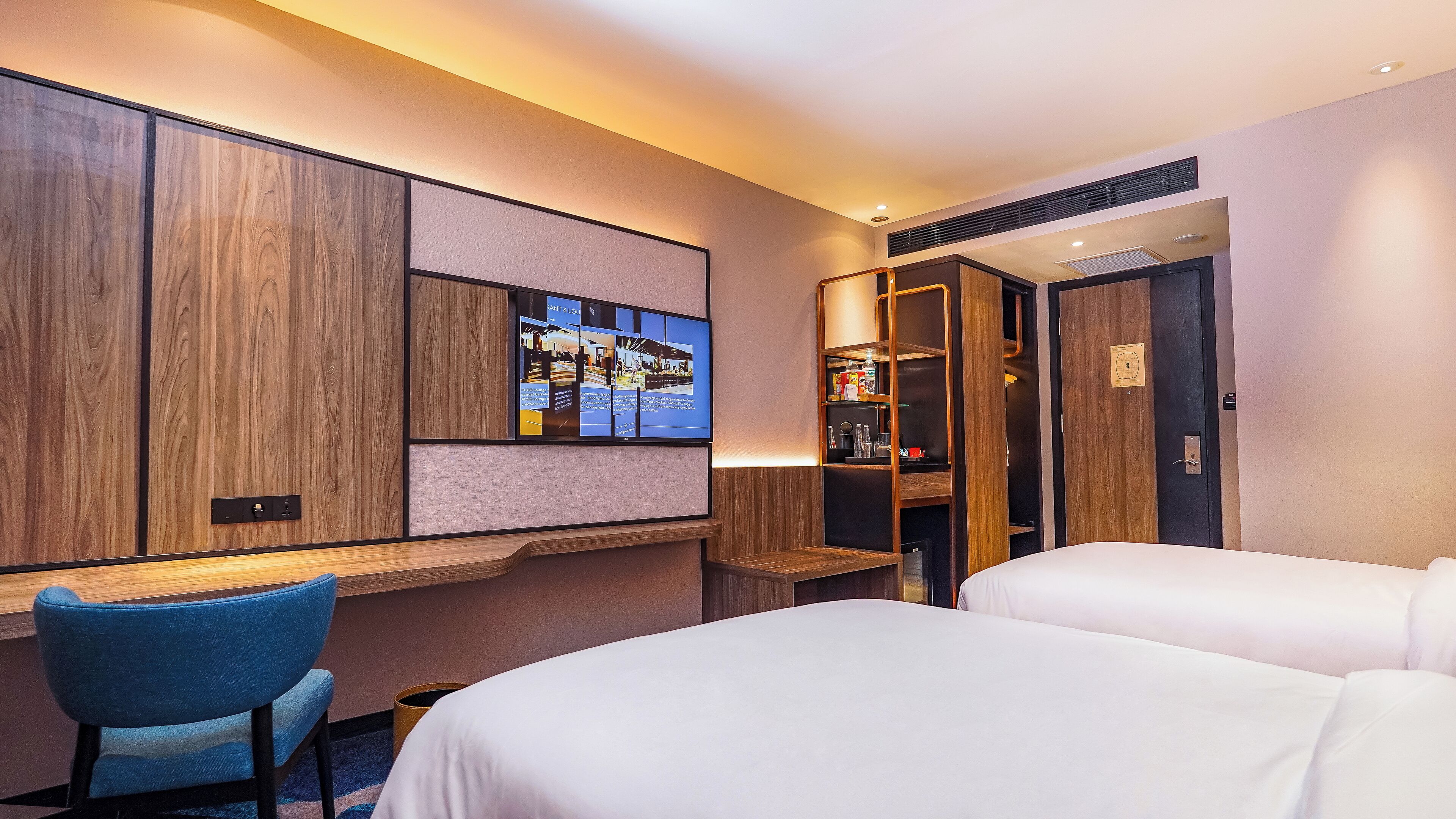 Een hotelkamer met een bureau, twee bedden, een televisie en een kledingkast.
